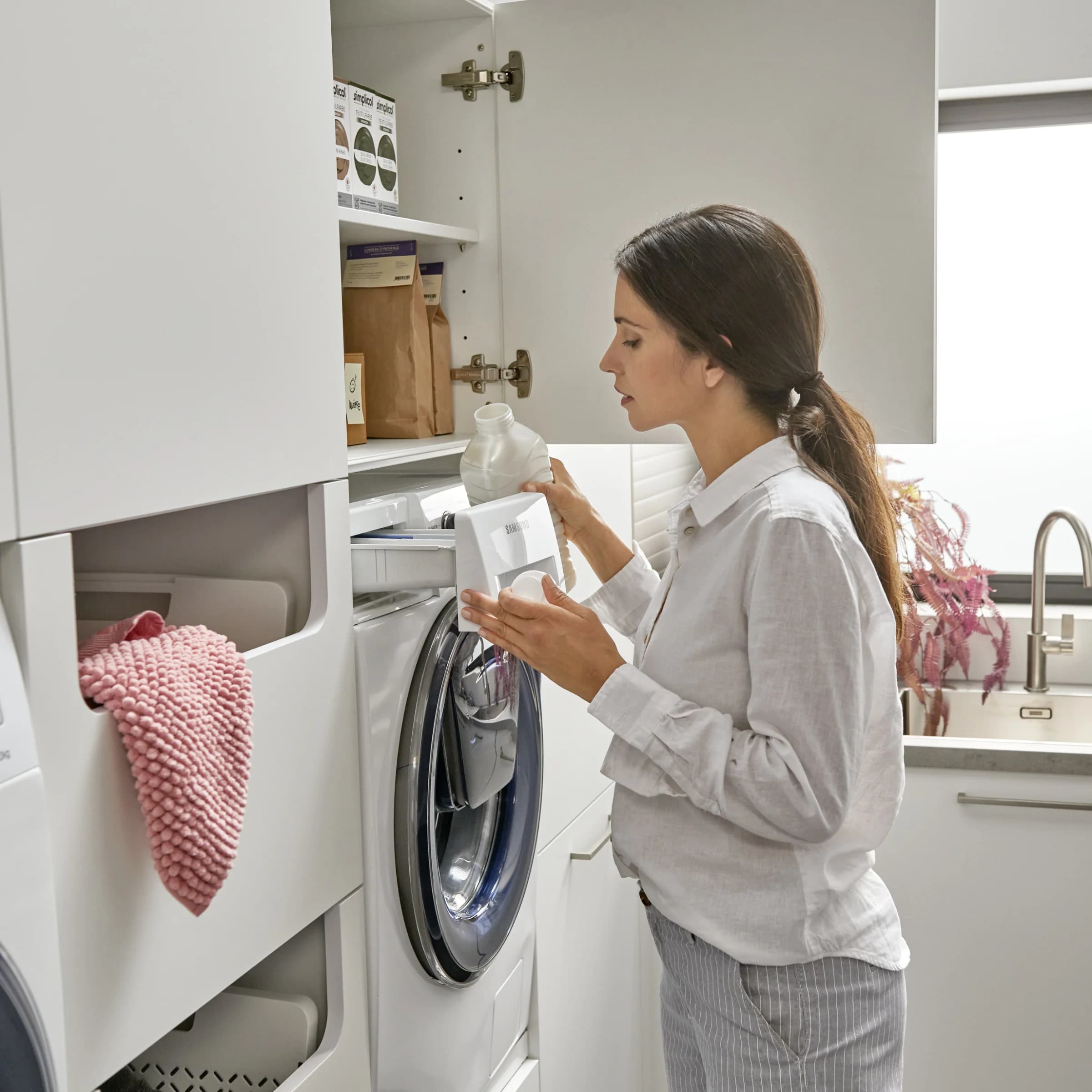 A woman operates a washing machine in a modern utility room by Nolte Utility Rooms.